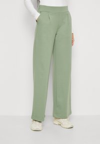 Pantalons larges vert clair en tissu doux et texturé avec une taille haute, comportant des poches latérales et des plis subtils pour plus de détails.