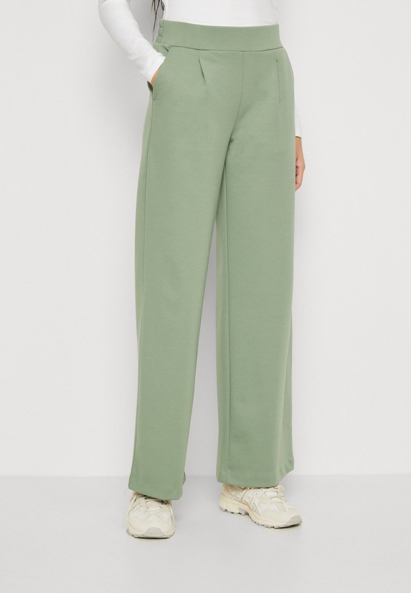 Pantalons larges vert clair en tissu doux et texturé avec une taille haute, comportant des poches latérales et des plis subtils pour plus de détails.