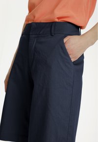 Pantaloni corti blu navy realizzati in tessuto misto cotone, con una silhouette dritta, tasche laterali e una texture liscia.