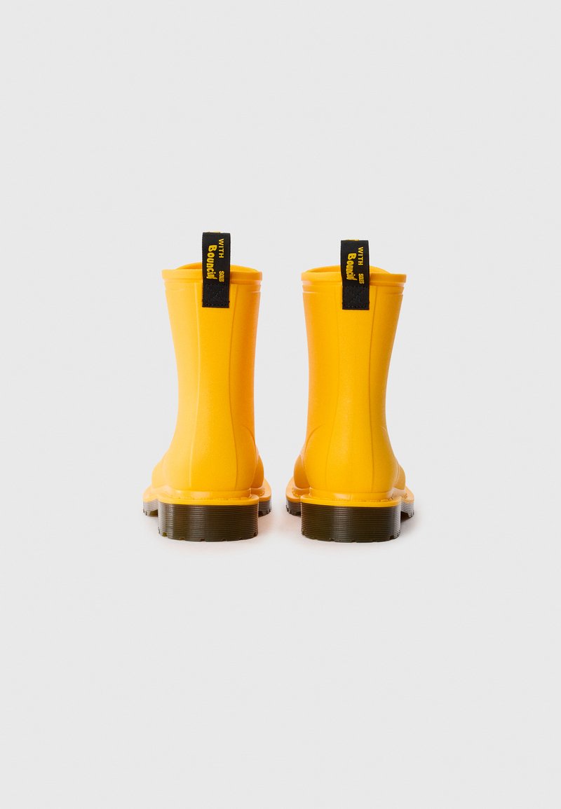 Yellow rubber ankle rain boots with a smooth texture, black accent pull tabs, and a low brown platform sole. Rear view highlighting shape.
