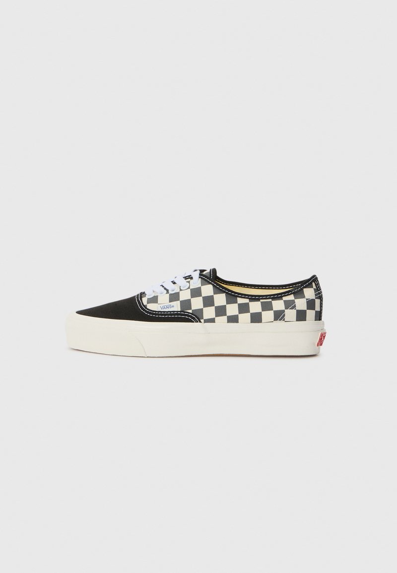 Black and white checkerboard canvas sneaker with a black toe cap, white laces, and cream rubber sole. Features Vans logo on the side.