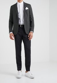 Dopasowana marynarka w czarno-białą kratę houndstooth, biała koszula z kołnierzykiem stójkowym, czarne spodnie, białe trampki, z poszetką i paskiem.