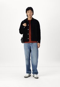 Black corduroy shirt jacket, red t-shirt, light blue jeans, white and black sneakers; black crossbody bag worn on shoulder.