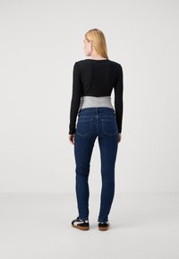 Top negro de manga larga con textura acanalada combinado con unos jeans ajustados de color azul oscuro. Los jeans tienen un diseño clásico de cinco bolsillos, y el conjunto se completa con zapatos informales.