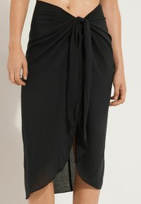 Jupe portefeuille noire en tissu léger. Dotée d'un détail de lien sur le devant, d'un ourlet asymétrique et d'une fente sur le côté pour un style supplémentaire.