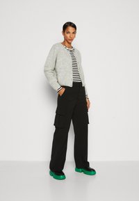 Gray, fluffy cardigan with buttons, layered over black and white striped top. Loose black cargo pants and chunky black and green platform shoes.