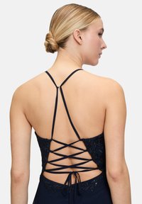 Robe marine avec des détails en dentelle complexes et des bretelles croisées dans le dos. Présente un corsage ajusté et une jupe fluide, accentuant la taille.