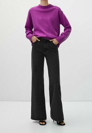 Lila gestrickter Pullover mit Rippbündchen und Knopfdetails, kombiniert mit hochtaillierten, weit geschnittenen schwarzen Jeans und schwarzen Sandalen mit offenem Zehenbereich.