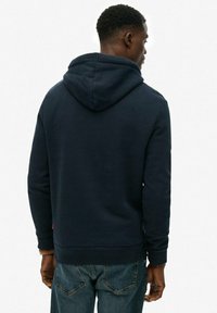 Granatowy hoodie z dużym, regulowanym kapturem; miękka tkanina; ściągacze przy rękawach i hemie; zawiera małe logo w pobliżu kieszeni.