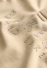 Beige katoenen stof met verhoogde, matte letters in een contrasterende kleur. De gladde textuur en subtiele glans verbeteren de zichtbaarheid van de ontwerpdetails.