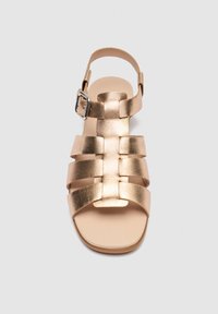 Arany bőrből készült lapos szandál több pánttal és ezüst csattal, felülről nézve, egyszerű háttér előtt.