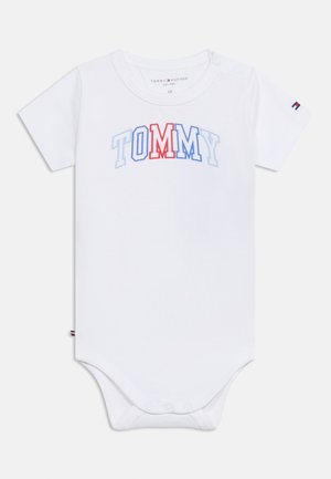 Weißer Baby-Body mit kurzen Ärmeln, mit "TOMMY" in roten und blauen Buchstaben auf der Brust bedruckt, mit Druckknöpfen unten und an der Schulter.