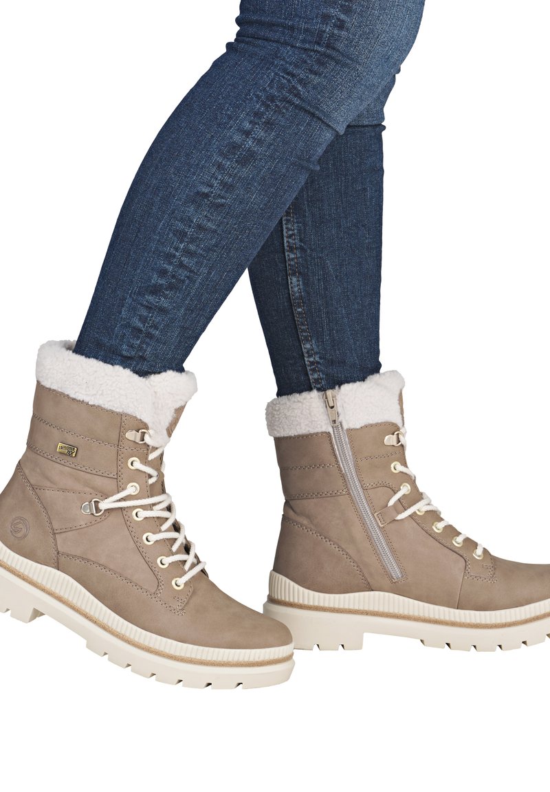 Braune Wildleder-Stiefeletten mit weißem Fellfutter, runder Zehenform, cremefarbener Sohle und seitlichem Reißverschluss; verfügen über ein geschnürtes Design und metallische Akzente.