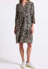 Leopardmönstrad klänning i beige och svart, med en v-ringning, trekvartslånga ärmar och en lagerdesign, kombinerad med vita sneakers.