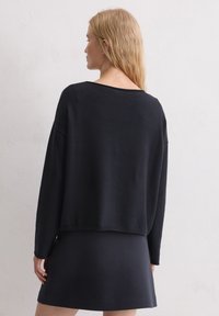 Zwarte sweatshirt met een losse pasvorm, ronde halslijn en lange mouwen, gecombineerd met een aansluitende zwarte rok. Zachte textuur, minimalistisch ontwerp.