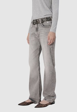 Grijze recht gesneden jeans met een vervaagde textuur, gecombineerd met een zwarte gesp met studs. Draagt een grijze top met lange mouwen en luipaardprint ballerina's.