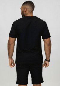 Ensemble de t-shirt et shorts de sport noir avec des rayures blanches sur les côtés, en tissu texturé. Le t-shirt a un design classique à col rond.