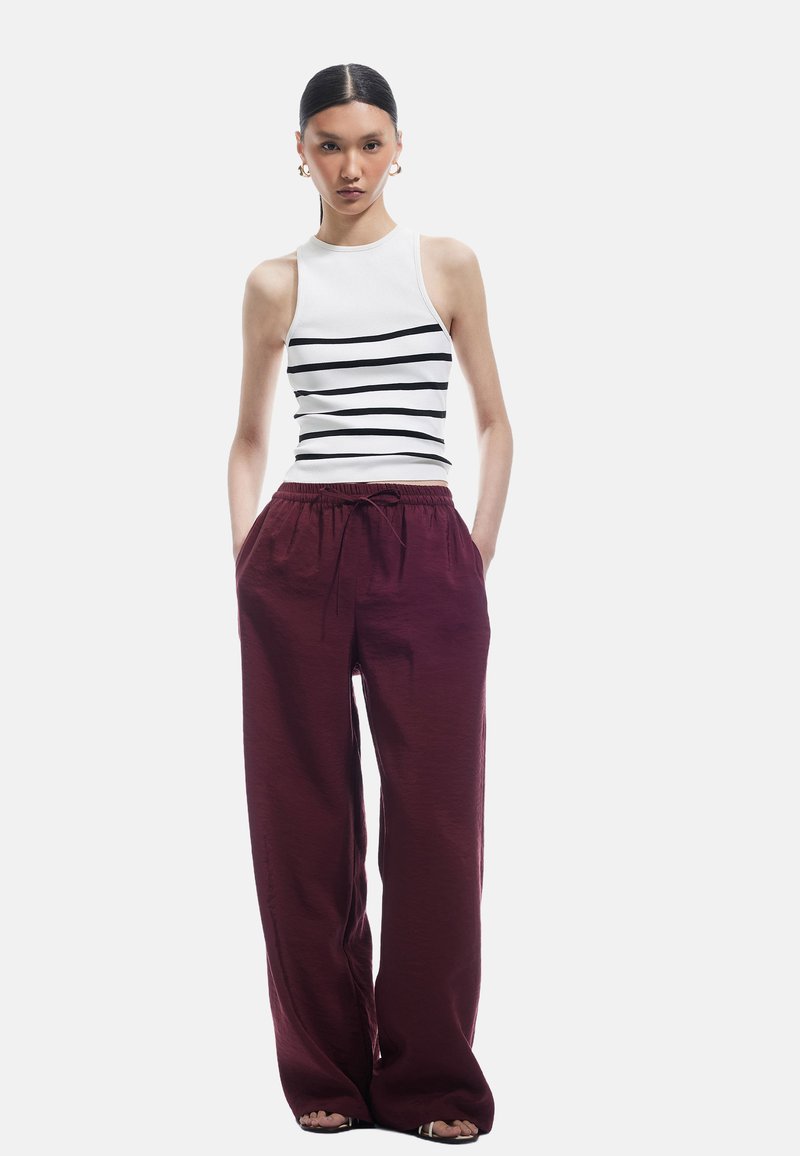 Top sans manches blanc avec des rayures horizontales noires, associé à un pantalon bourgogne ample avec une taille élastique et un cordon de serrage.