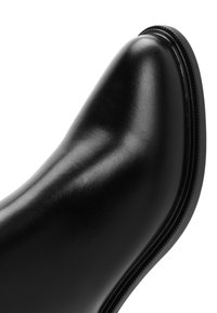 Botín de cuero negro hasta el tobillo con punta redonda, superficie lisa y suela de goma delgada con un borde texturizado.