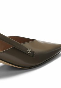 Scarpa fegato in vernice con punta affusolata, dotata di un sottile cinturino e di un accento con logo argentato. La texture liscia e il design elegante enfatizzano l'eleganza.