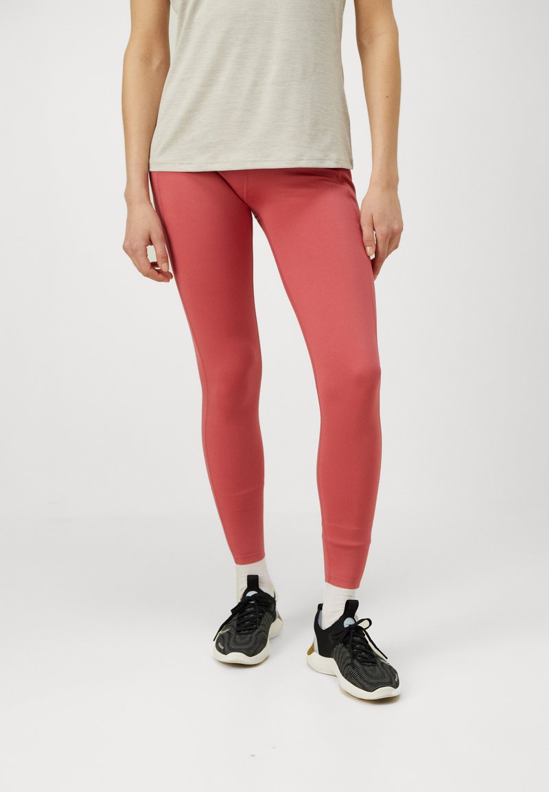 Rózsaszín leggings rugalmas anyagból, testhezálló kivitelben és boka hosszan. Fekete sportcipővel és világosszürke felsővel párosítva.