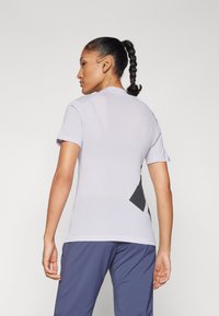 Camisola atlética feminina leve em roxo com mangas curtas, apresentando um painel de malha nas costas para respirabilidade e detalhes geométricos pretos.