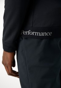 Veste de sport noire à texture lisse, avec un logo argenté "Performance" sur la ceinture et une coupe ajustée.