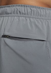 Gros plan sur un short de sport gris avec une taille élastique, une poche arrière zippée horizontale et un texte brodé "DRI-FIT".