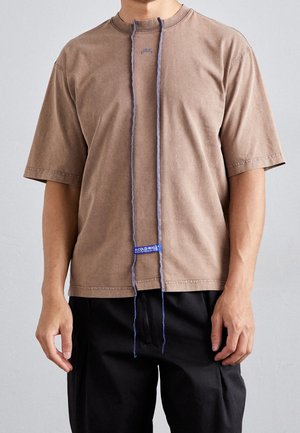 Bruine T-shirt met korte mouwen en een ronde hals, voorzien van een paarse verticale koorddetail en een blauw logolabel aan de zoom.