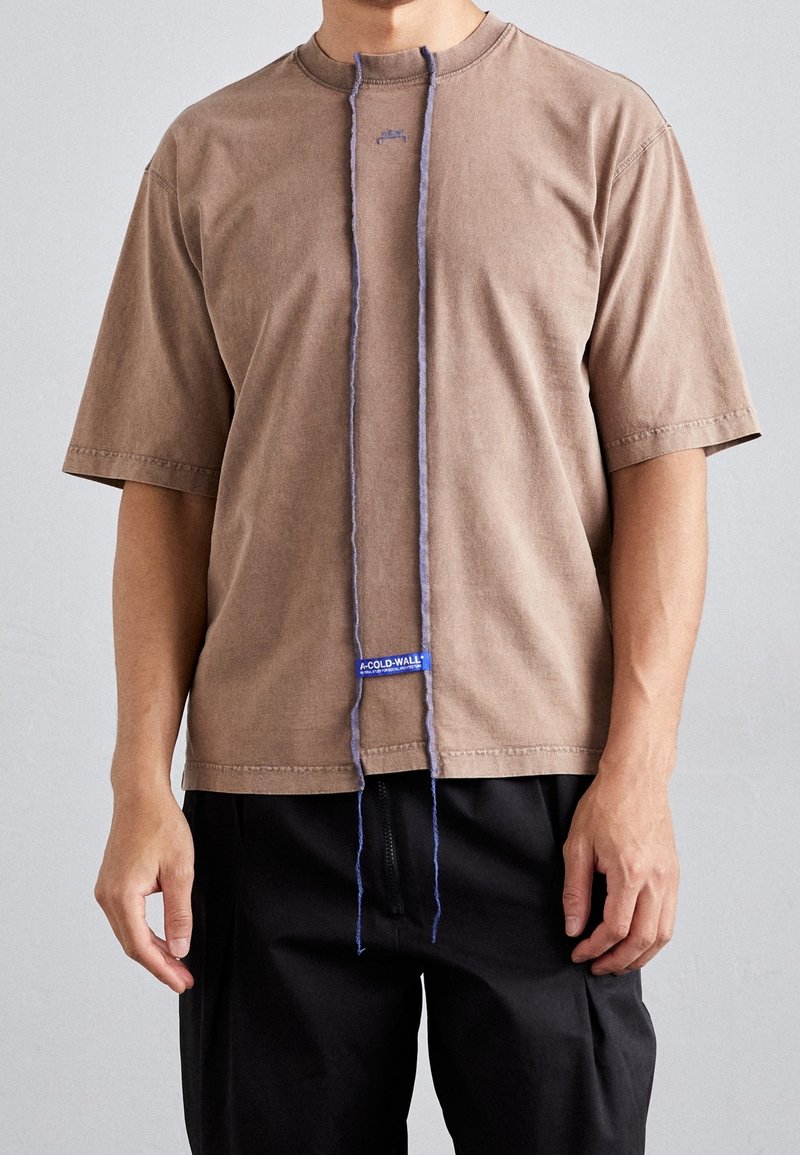 T-shirt marron à manches courtes avec un col rond, présentant un détail de cordon vertical violet et une étiquette de logo bleue à l'ourlet.
