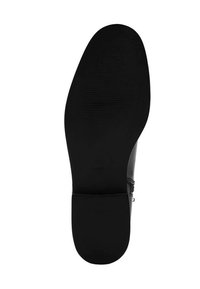 Suela de zapato negra con agarre texturizado. Presenta una forma suave y redondeada y un tacón plano. Construida con material de goma con logo de la marca en relieve.