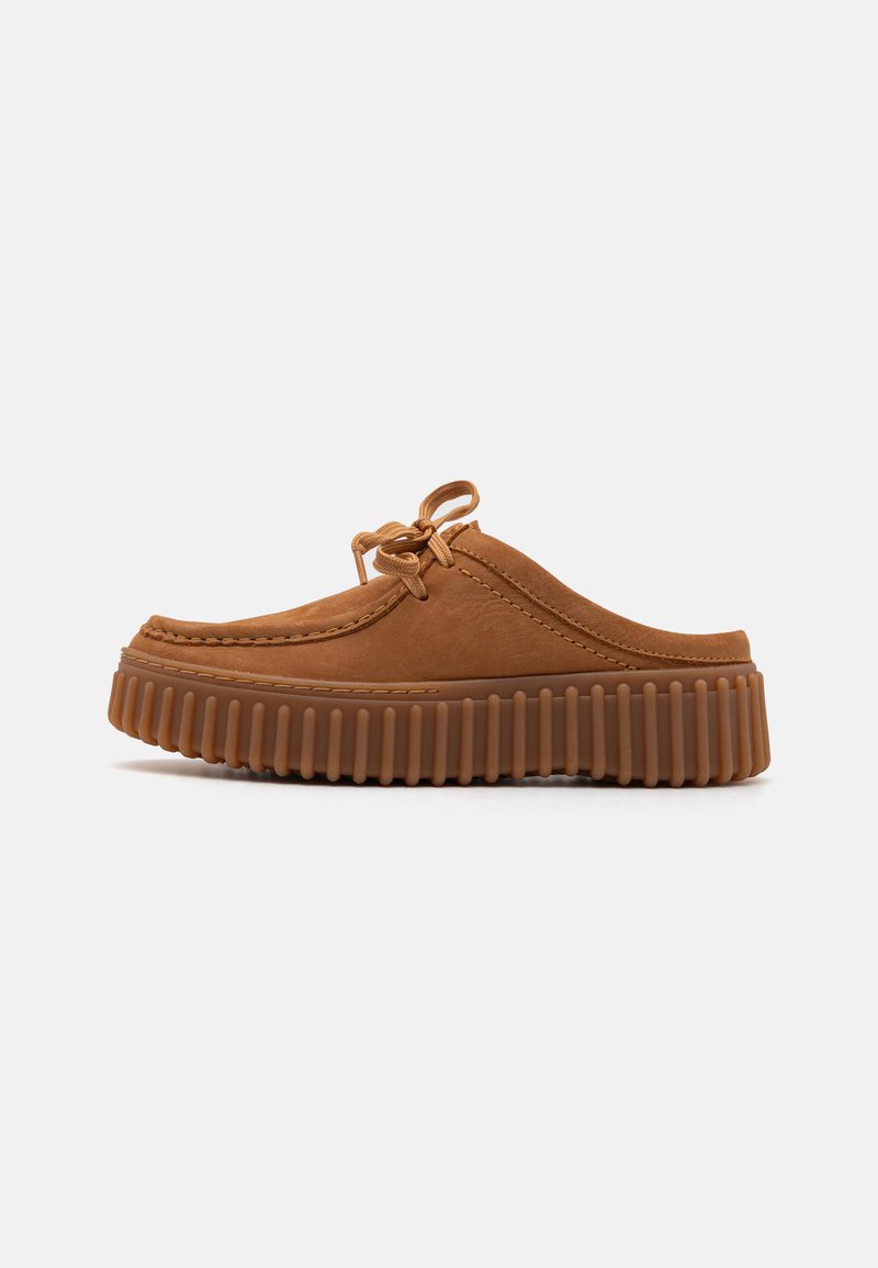 Brown suede slip-on shoe with a ribbed rubber sole, lace detail, and rounded design. Features stitching along the upper edges.