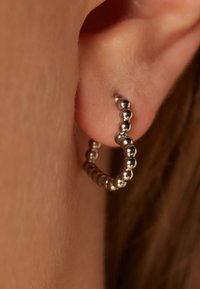 Zilveren oorbel met een kralenontwerp, die een glanzende, gladde textuur en een cirkelvorm toont, gedragen in een gepierced oor.