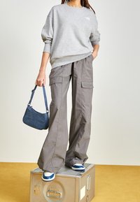 Šedá mikina, široké šedé cargo kalhoty, modrá taška přes rameno a námořnické tenisky. Neformální outfit s oversize střihem a praktickými kapsami.