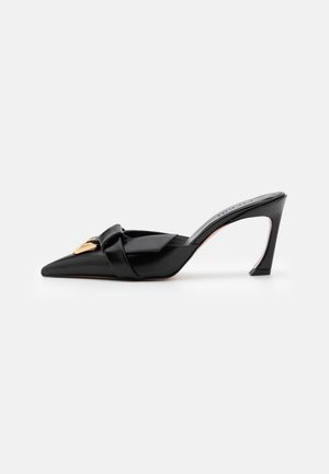 Black patent leather mules with a pointed toe, knotted front design, gold-tone hardware, and a tapered high heel.