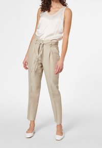 Beige randiga byxor med hög midja och justerbart knytbälte, tillsammans med en ljus satin tanktop med v-ringning och vita klackskor.