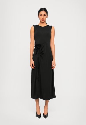 Vestito nero senza maniche con busto aderente e dettaglio drappeggiato in vita, caratterizzato da un accento floreale. Lunghezza midi con una texture liscia.