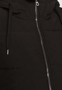 Schwarze gesteppte Jacke mit einem silbernen Reißverschluss und schwarzen Kordeln, die den oberen Oberkörperbereich und die Verschlussdetails zeigt.