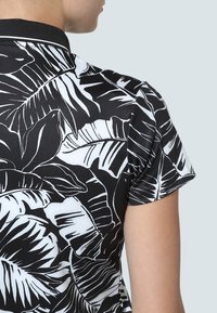 Kratký rukáv košile s černobílým tropickým vzorem listů, sportovním límcem a hladkým, lehkým textilem.