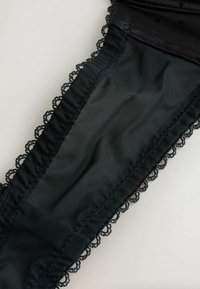 Black lingerie garter with a blend of smooth material and sheer mesh. Features delicate lace trim along the edges.