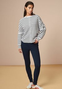 Maglietta a maniche lunghe a righe in bianco e blu navy, con bottoni frontali e vestibilità morbida, abbinata a jeans skinny scuri e sneaker bianche.