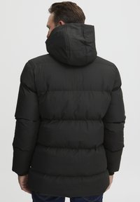 Melnā pildīta jaka ar kapuci, kurai ir quilted dizains un elastīgas aproces, izgatavota no gludas, ūdensizturīgas materiāla.