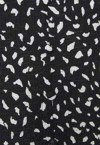 Tessuto nero con una superficie texture che presenta forme e schemi bianchi irregolari, creando un contrasto di colori e un effetto visivo dinamico.