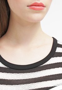 Top rayé noir et blanc avec une texture en dentelle, un col rond élégant avec une bordure noire unie et un aperçu rapproché de la zone du col.