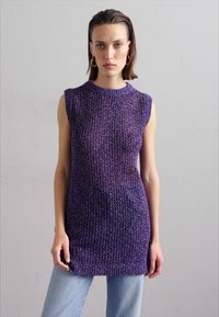 Adīta bezpiedurkņu blūze gradient violetos toņos, ar teksturētu rakstu, apaļu dekoltē un pagarinātu siluetu, kombinēta ar gaišām džinsiem.