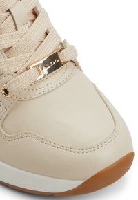 Lichtbeige sneaker met een gladleren bovenkant, tonale stiksels en goudkleurige hardware. Beschikt over een gecushioneerde zool en gestructureerde veters.