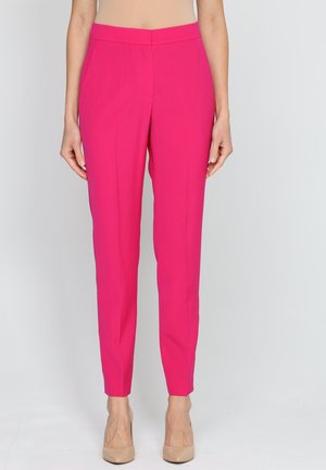 Dopasowane różowe spodnie o gładkiej teksturze, zwężane nogawki i boczne kieszenie. Stylizowane z neutralnymi szpilkami.
