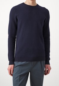 Mörkblå stickad tröja med ett strukturerat mönster, rund halsringning och ribbade ärmslut och nederkant. Kombinerad med ljusblå byxor.