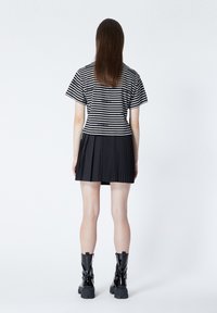 Randig svart och vit topp med korta ärmar, tillsammans med en svart plisserad kjol. Modellen bär blanka svarta kängor.