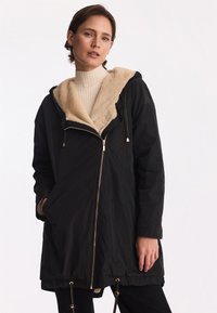 Czarna parka z futrzanym wykończeniem i kapturem, z zamkiem z przodu, sznurkami w talii oraz bocznymi kieszeniami.